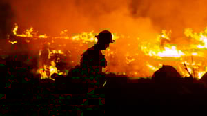 Photo of firefighter silhouetted against fire in background.